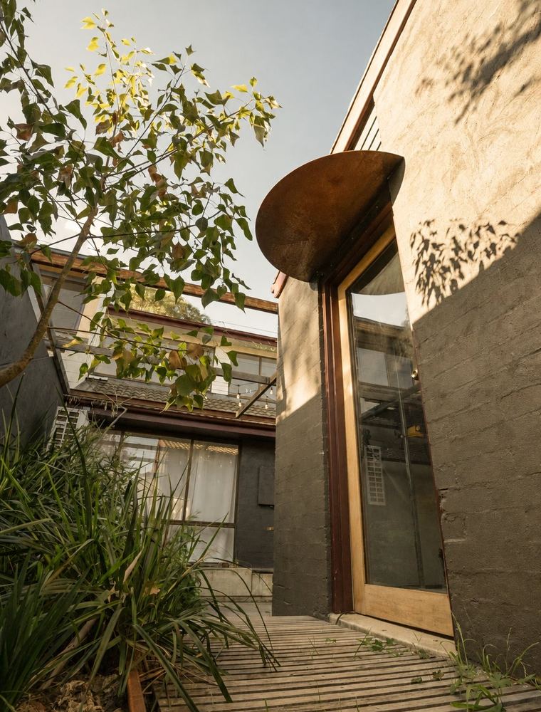 Connelly Place courtyard — corten steel awning over the entry, timber walkway through grasses