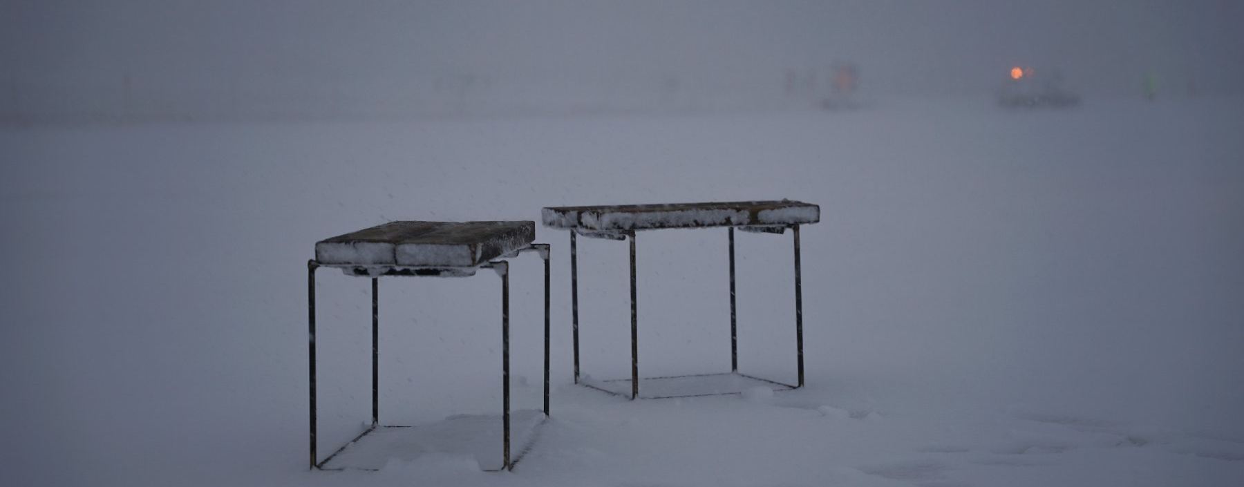 Two frost-covered stone tables, alone in a snow field at dusk